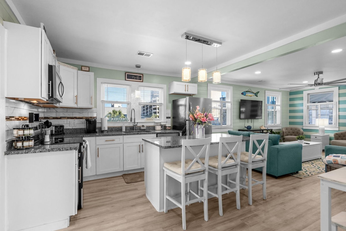 Bright white kitchen with granite island, breakfast-bar seating and pendant lights, open to the living room